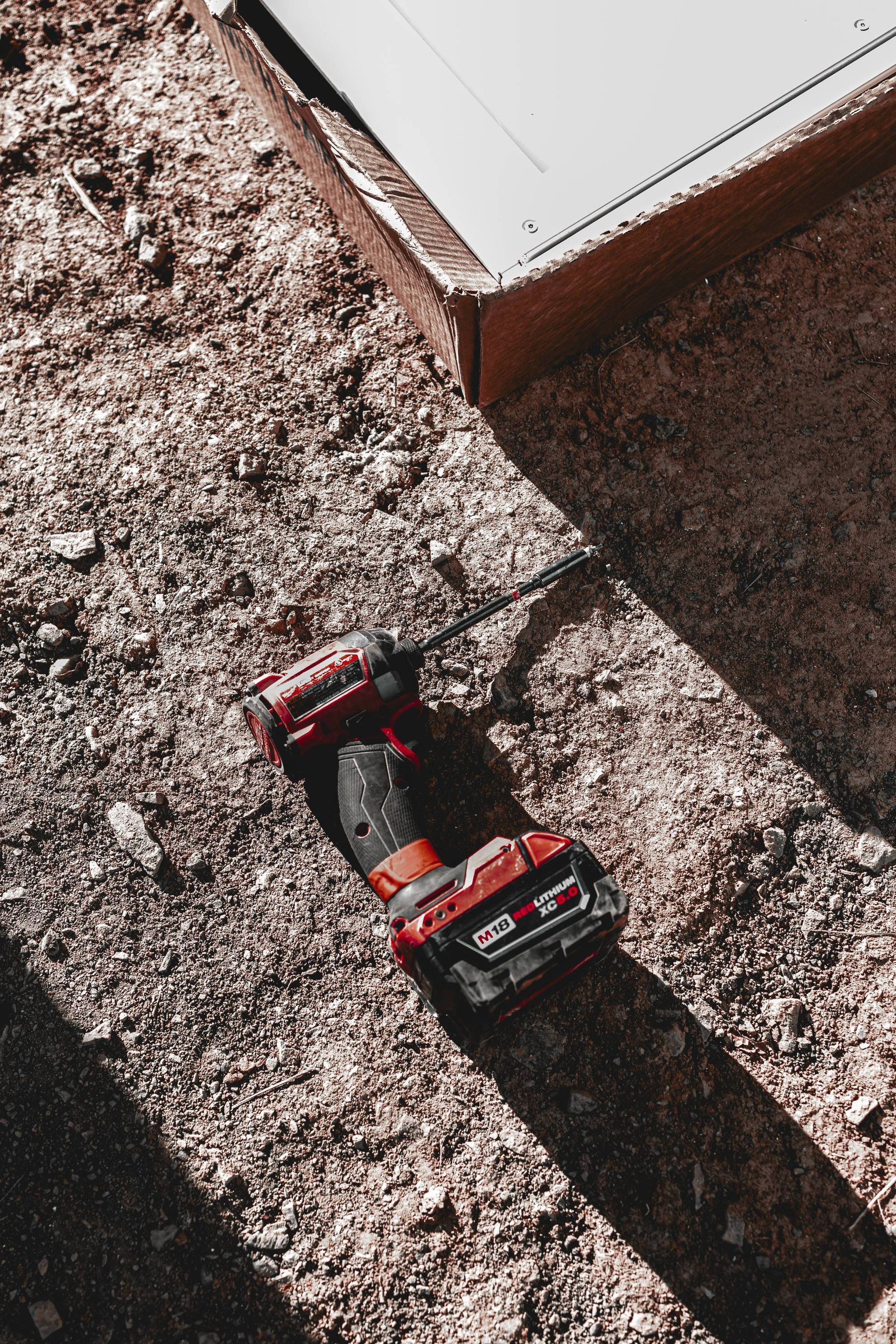 Red drill on a ground with wood chips, near a wooden structure.