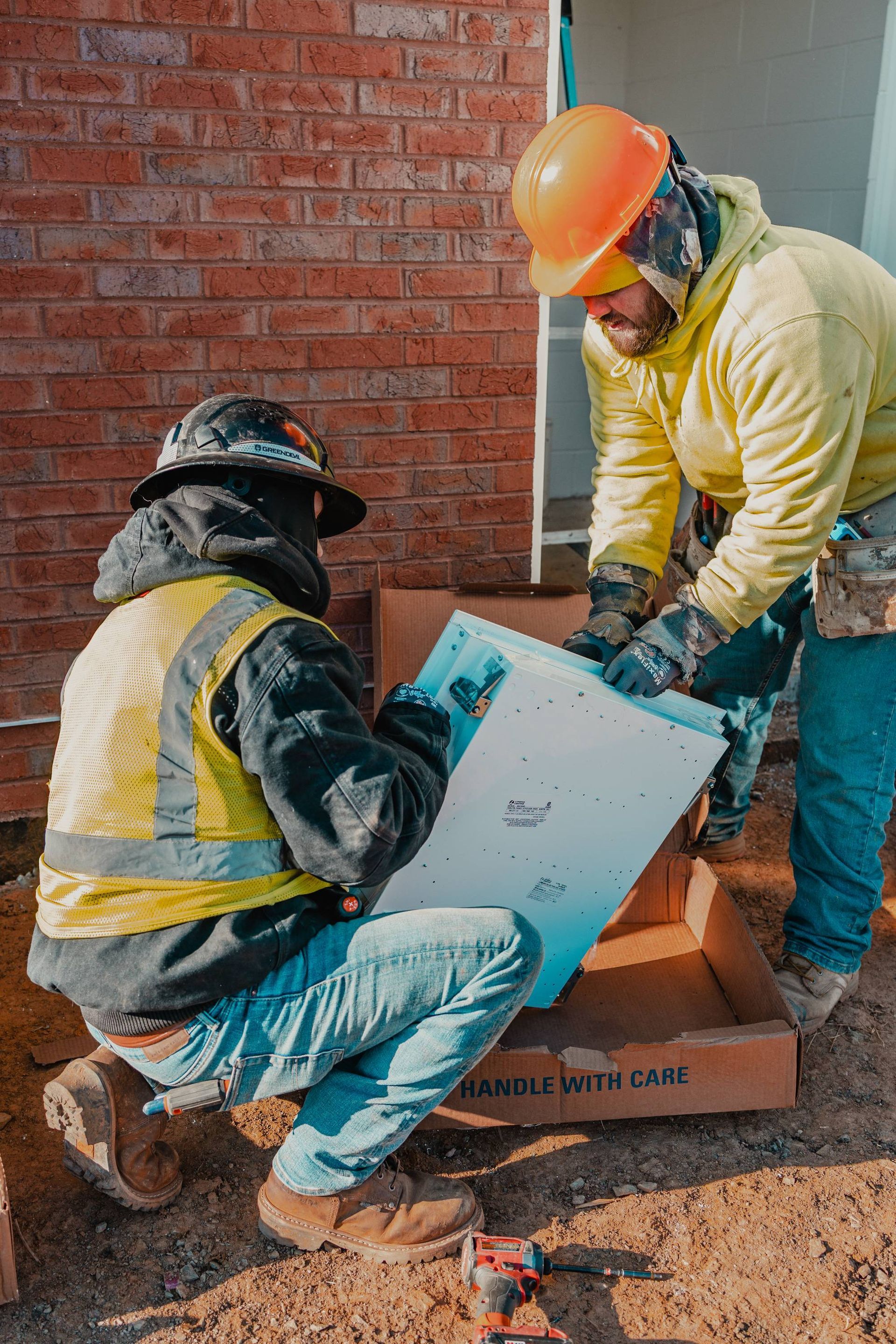 Construction workers examining blueprints at a brick building site, wearing hard hats and workwear.