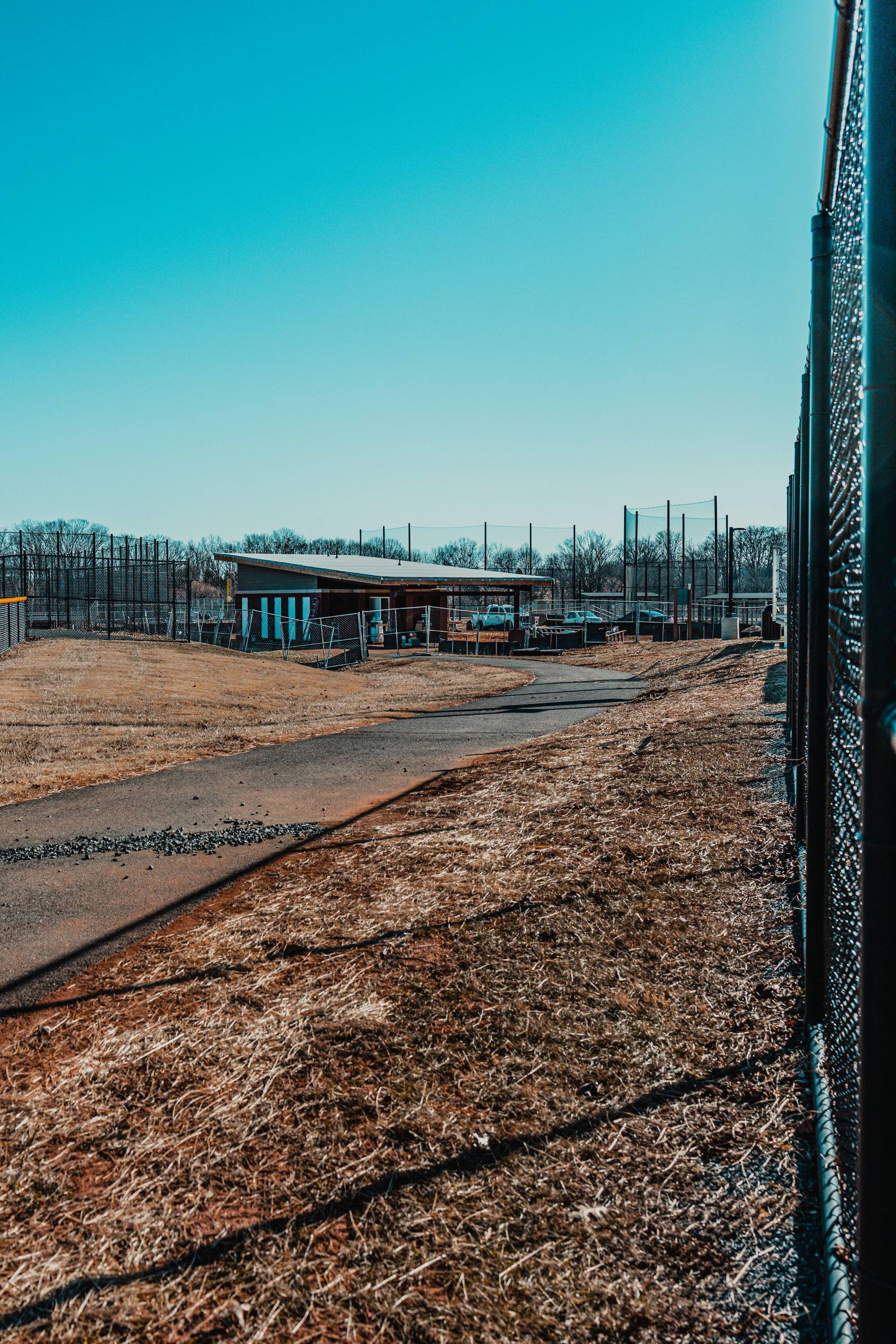 Fence with a gravel path, leading to a building under a clear blue sky.