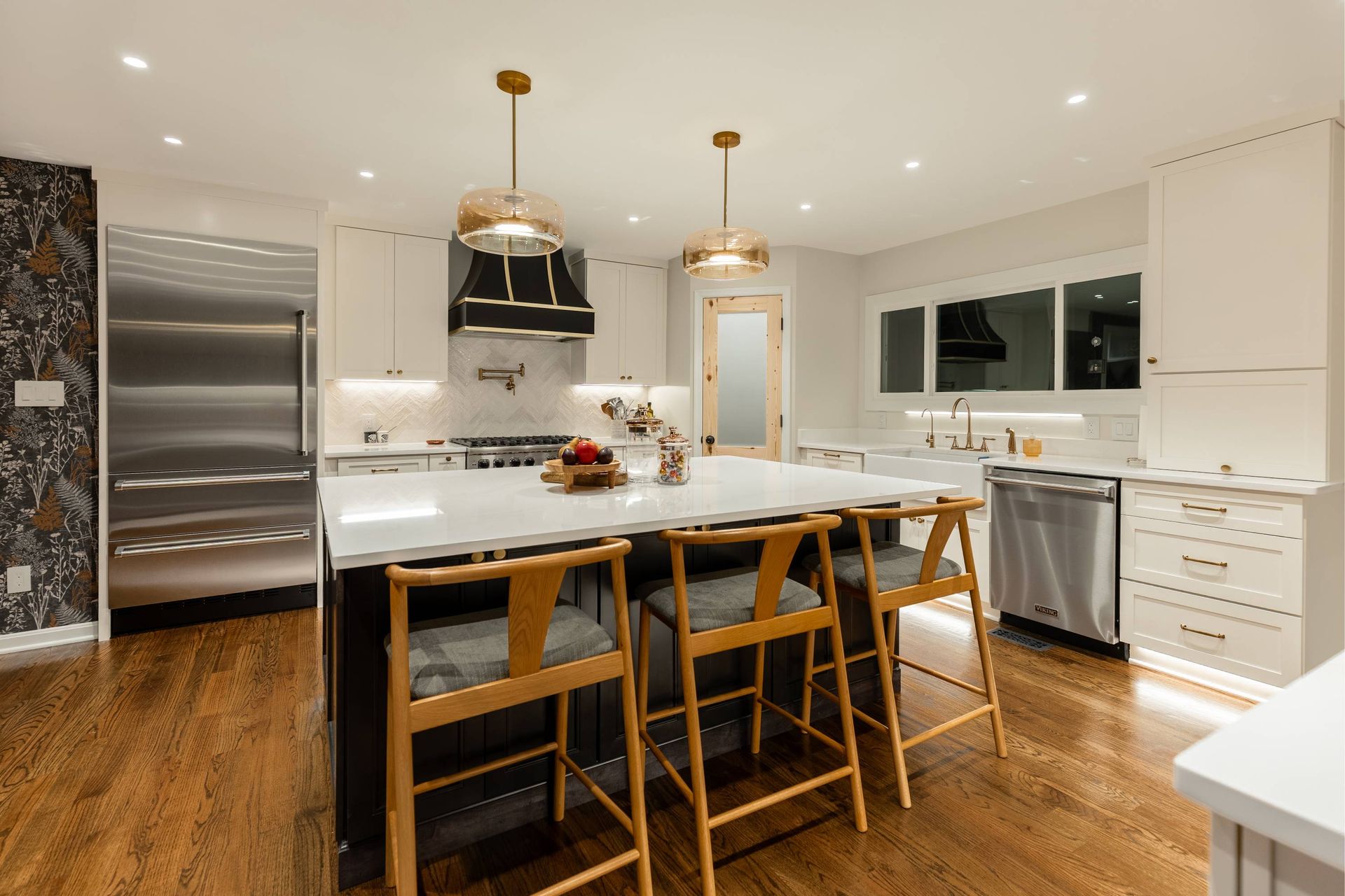 Modern kitchen with white cabinets, dark island with barstools, stainless steel appliances, and gold pendant lights.