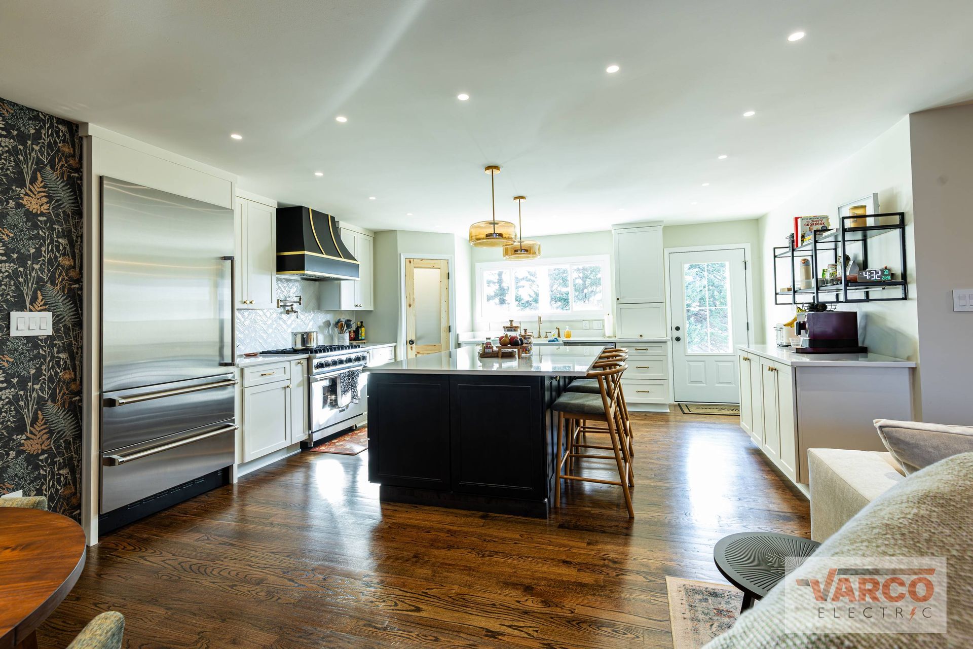 Spacious kitchen with dark island, stainless steel appliances, white cabinets, and wood flooring.
