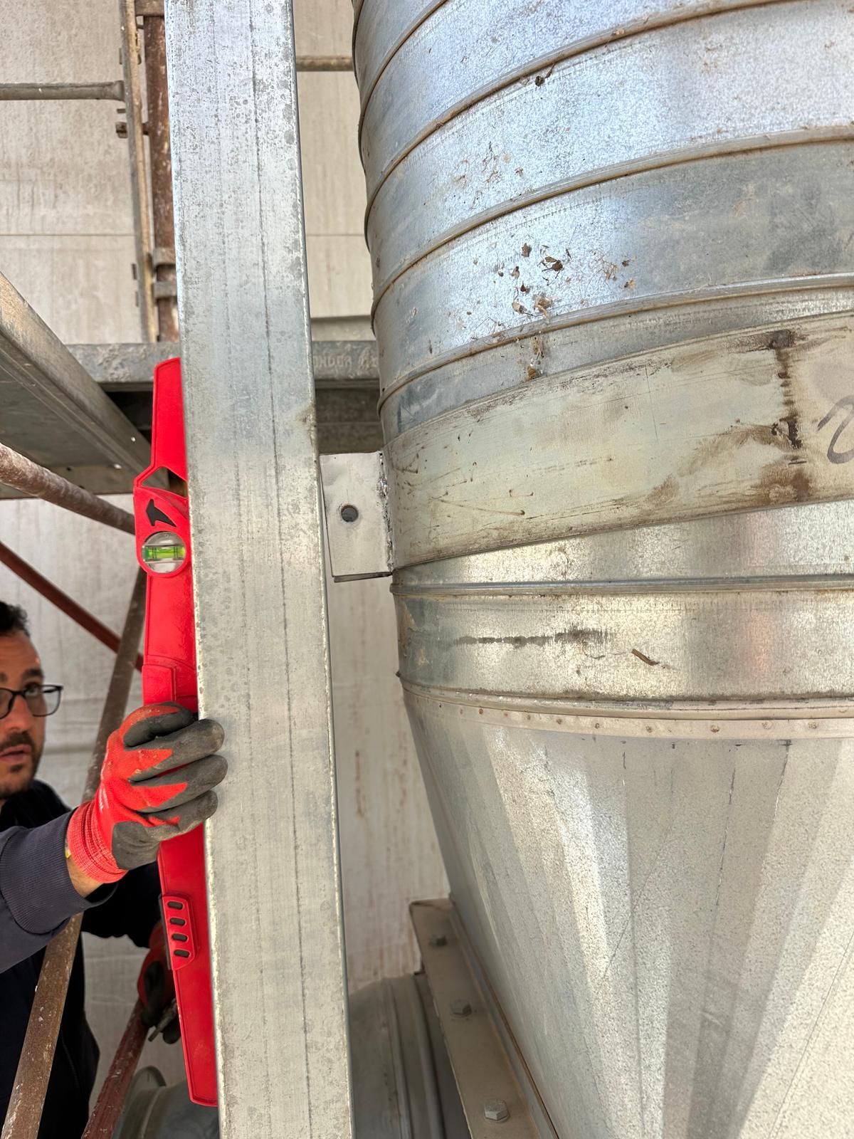Operaio con una livella rossa accanto a un grande condotto metallico argentato in un ambiente industriale
