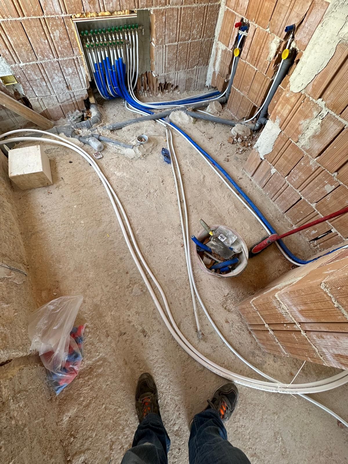 Stanza in fase di costruzione con pareti in mattoni a vista e cavi elettrici blu e bianchi sul pavimento.