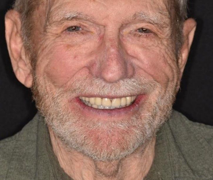 Smiling older man with a beard, wearing a green shirt, and a black background.