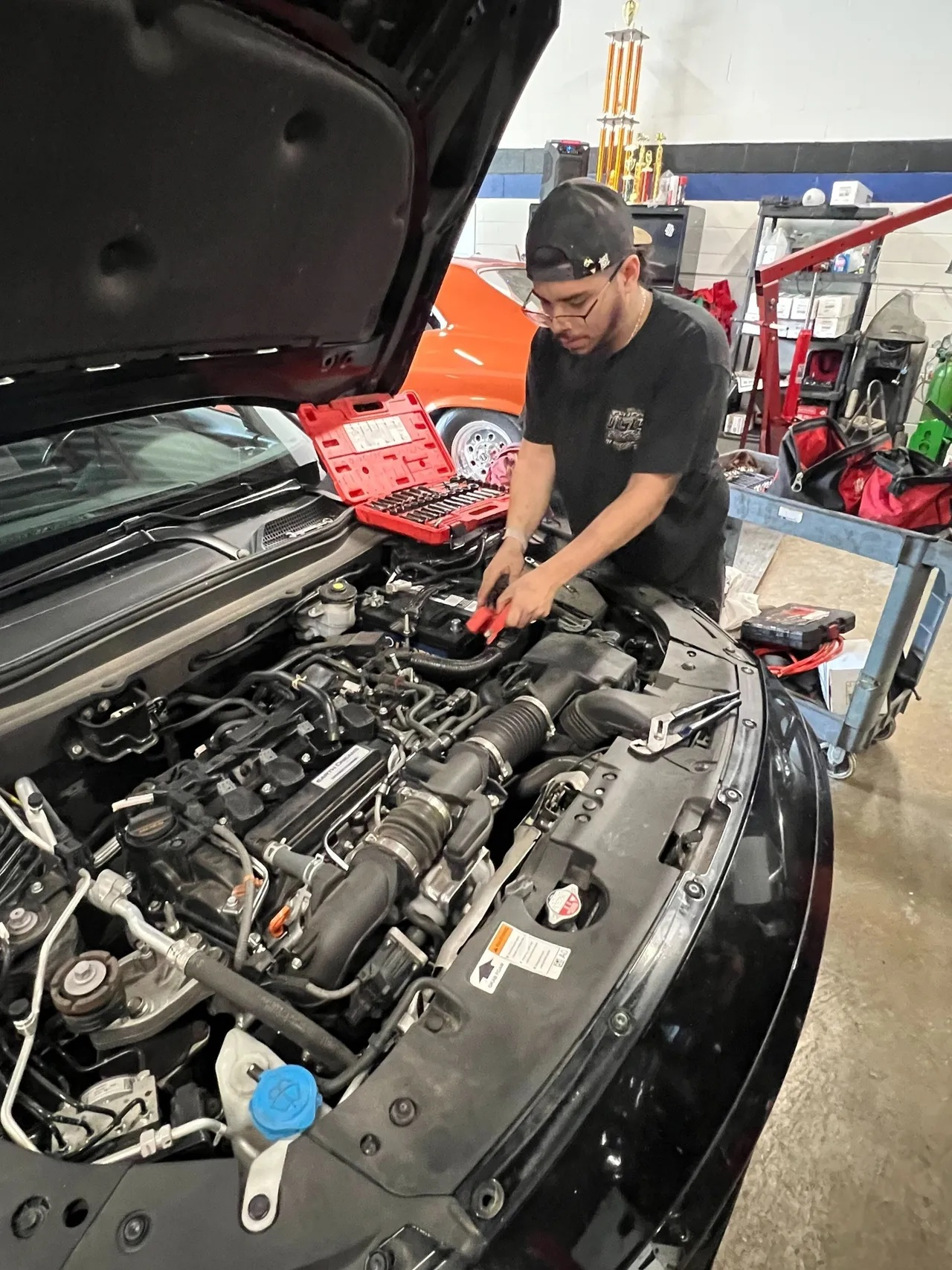 Mechanic working on car engine in a garage with open hood. | Ashten's Total Auto Care