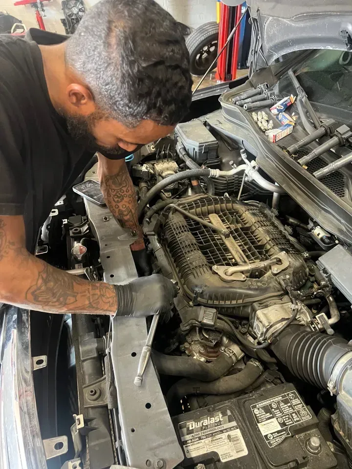 Mechanic working on a car engine in a garage. He wears gloves and uses a tool. | Ashten's Total Auto Care