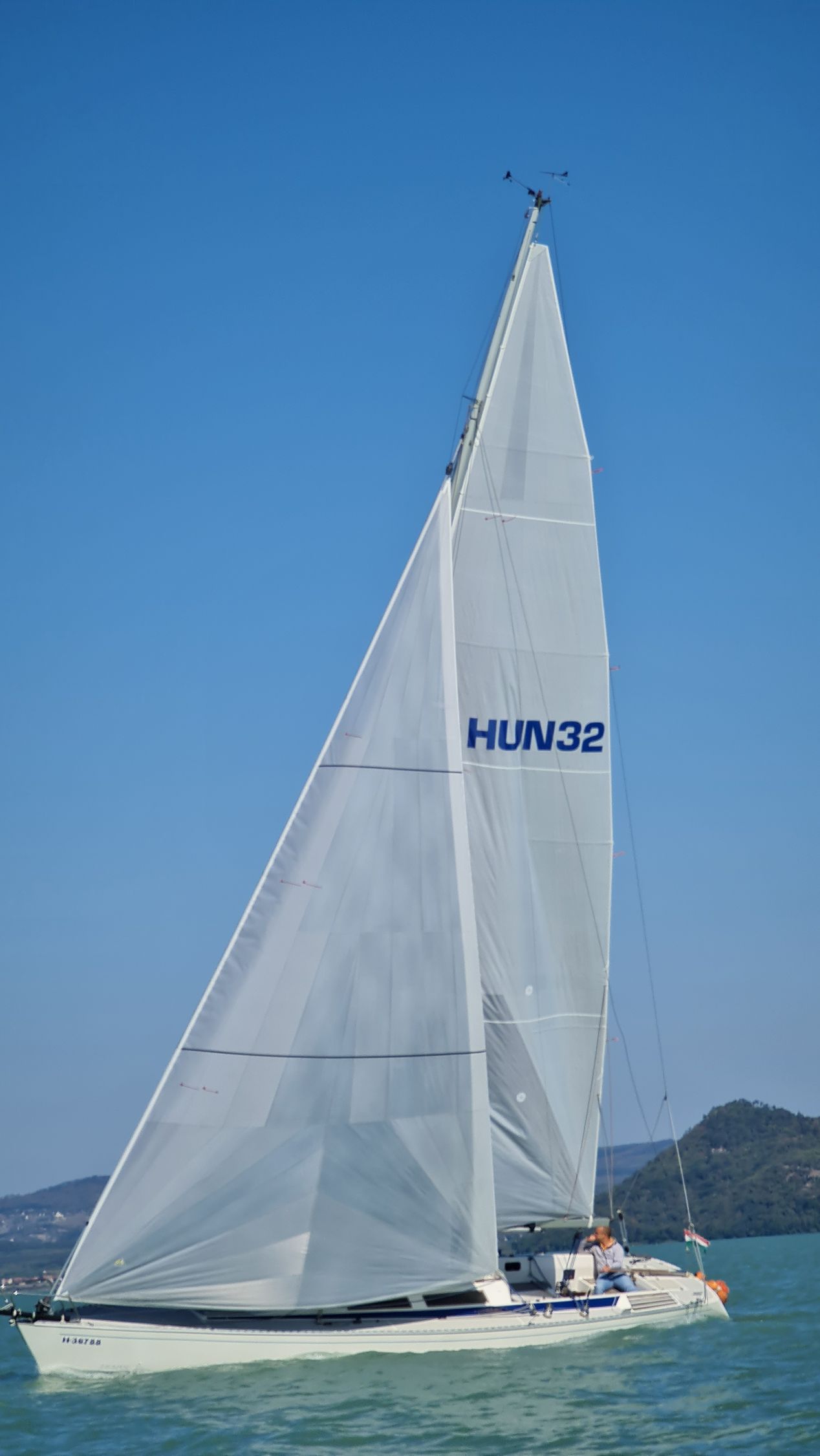 Sailboat with full white sail on a blue lake; 