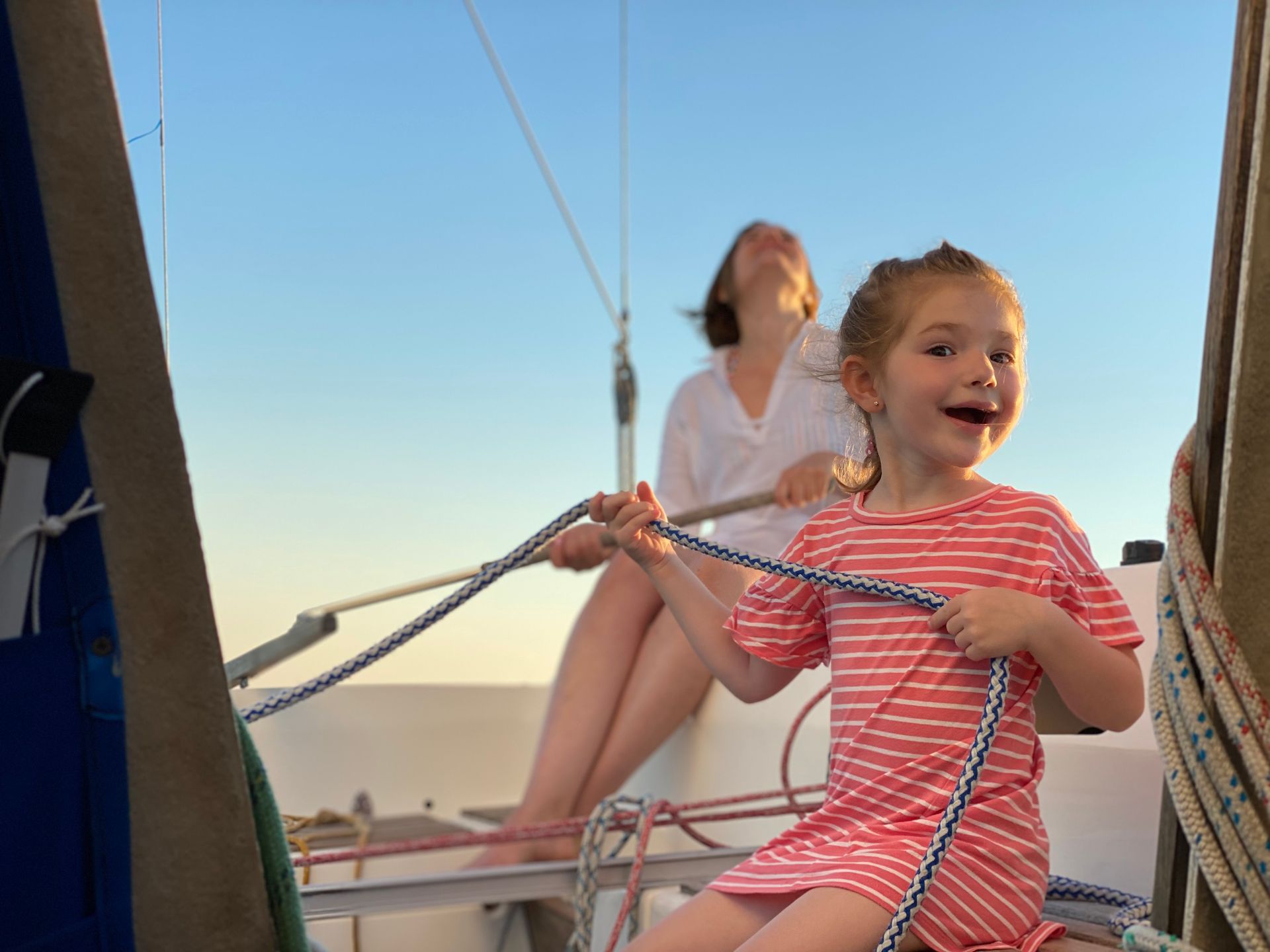 Girl and woman sailing, girl smiling holding rope, blue sky.