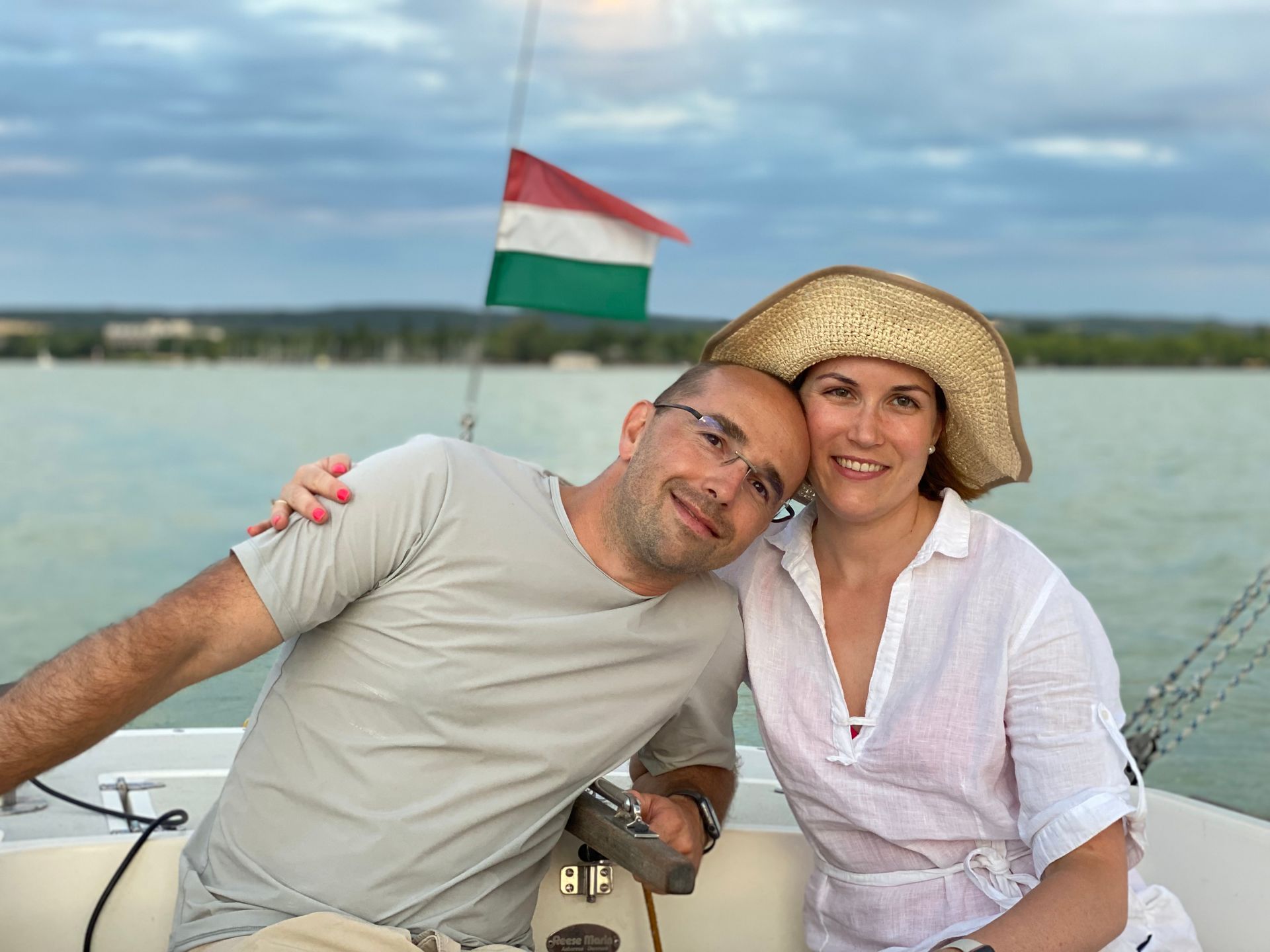 A man and woman on a boat with Hungarian flag, man leaning on woman's shoulder.