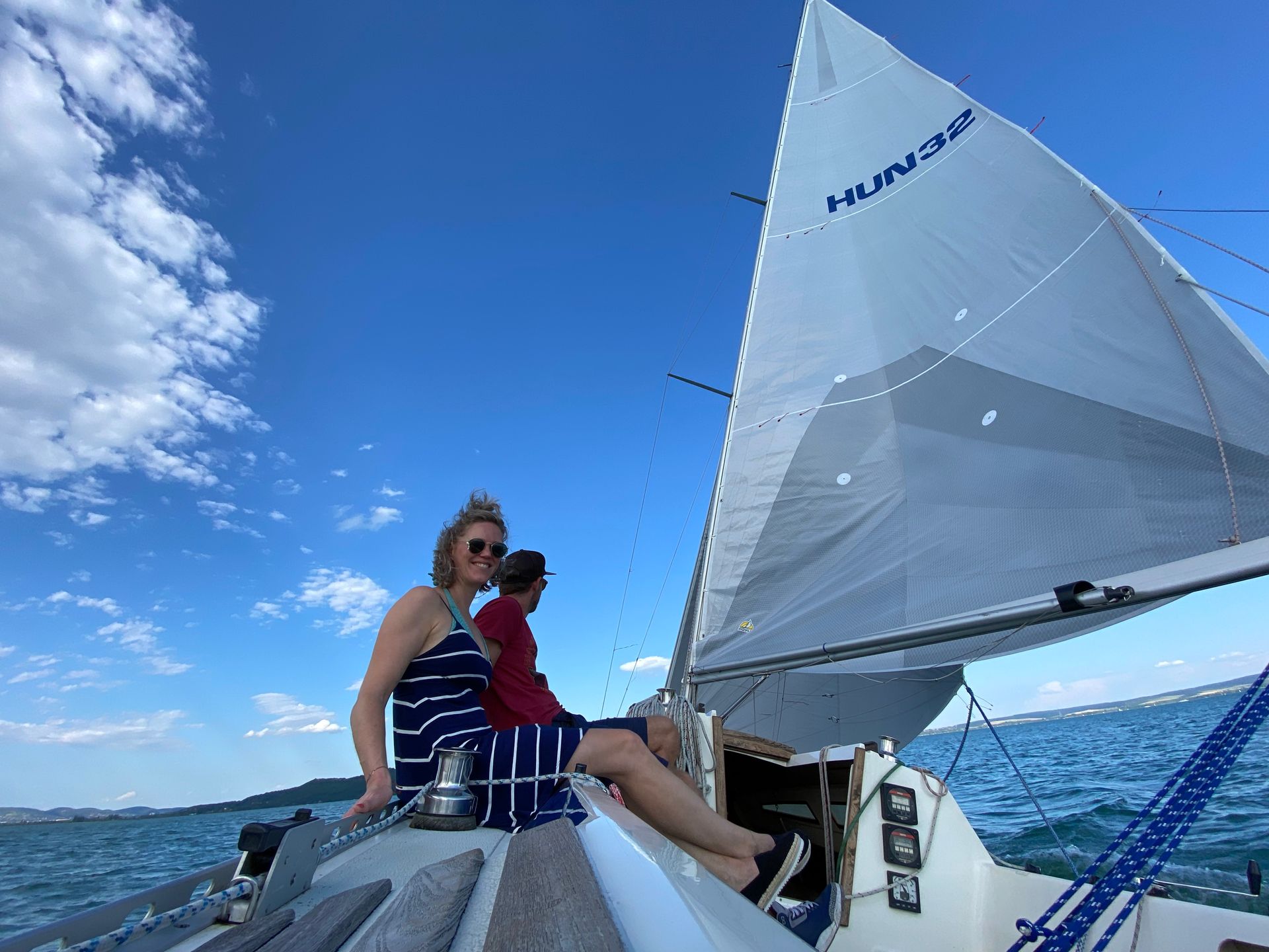 Woman and man on a sailboat with a white sail against a blue sky.