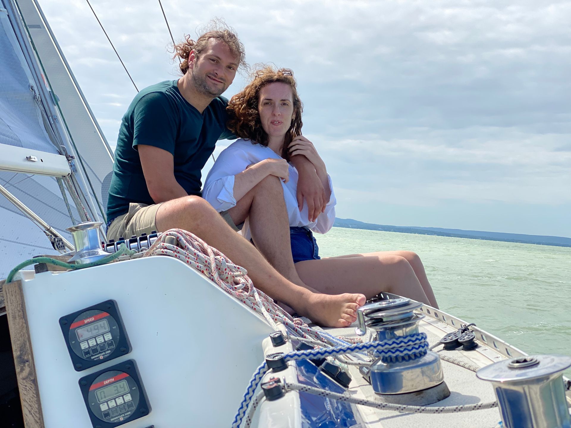 Couple on a sailboat, smiling, with water and sky in the background.