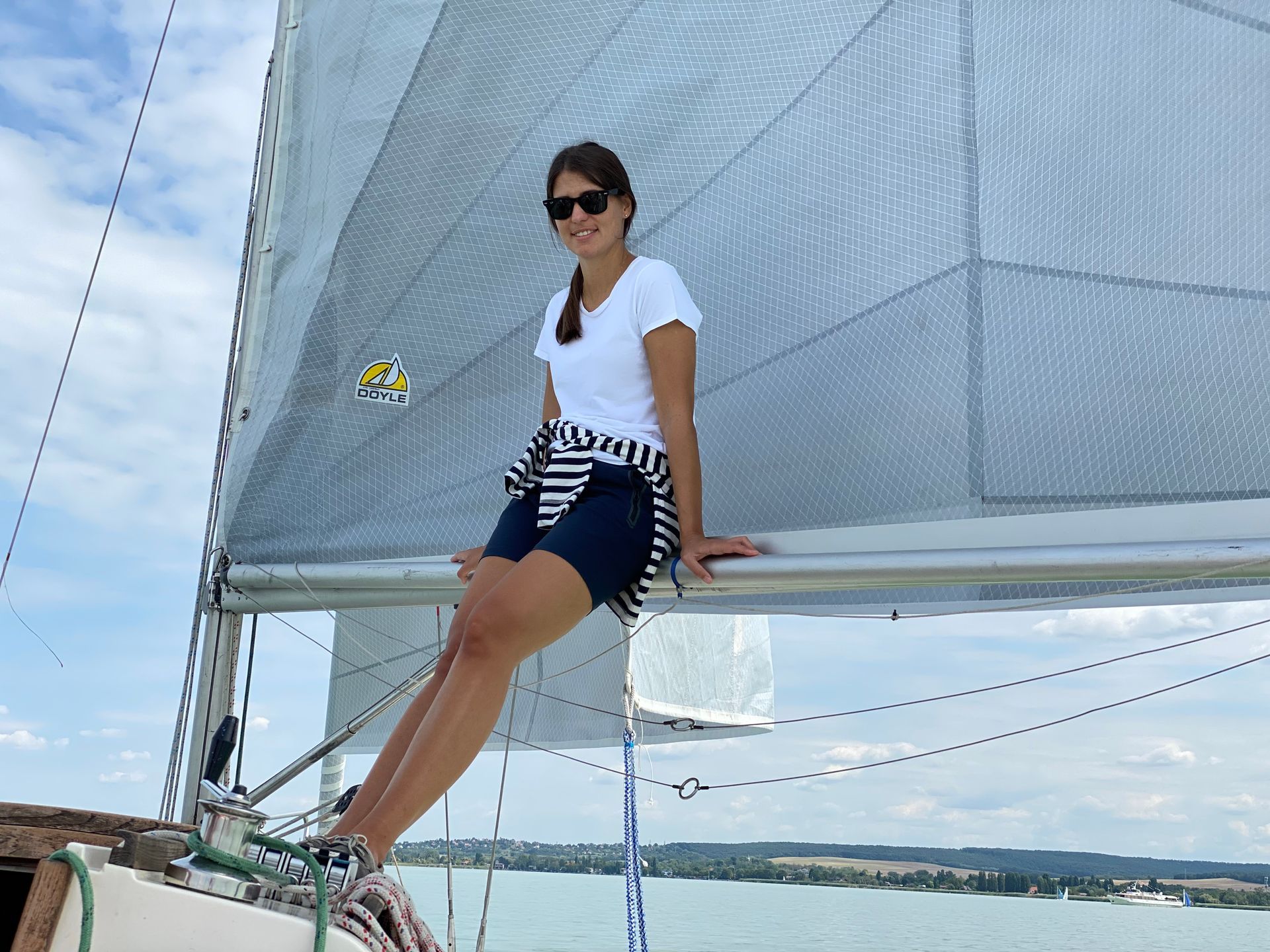 Woman in sunglasses sits on a sailboat, smiling at the camera.