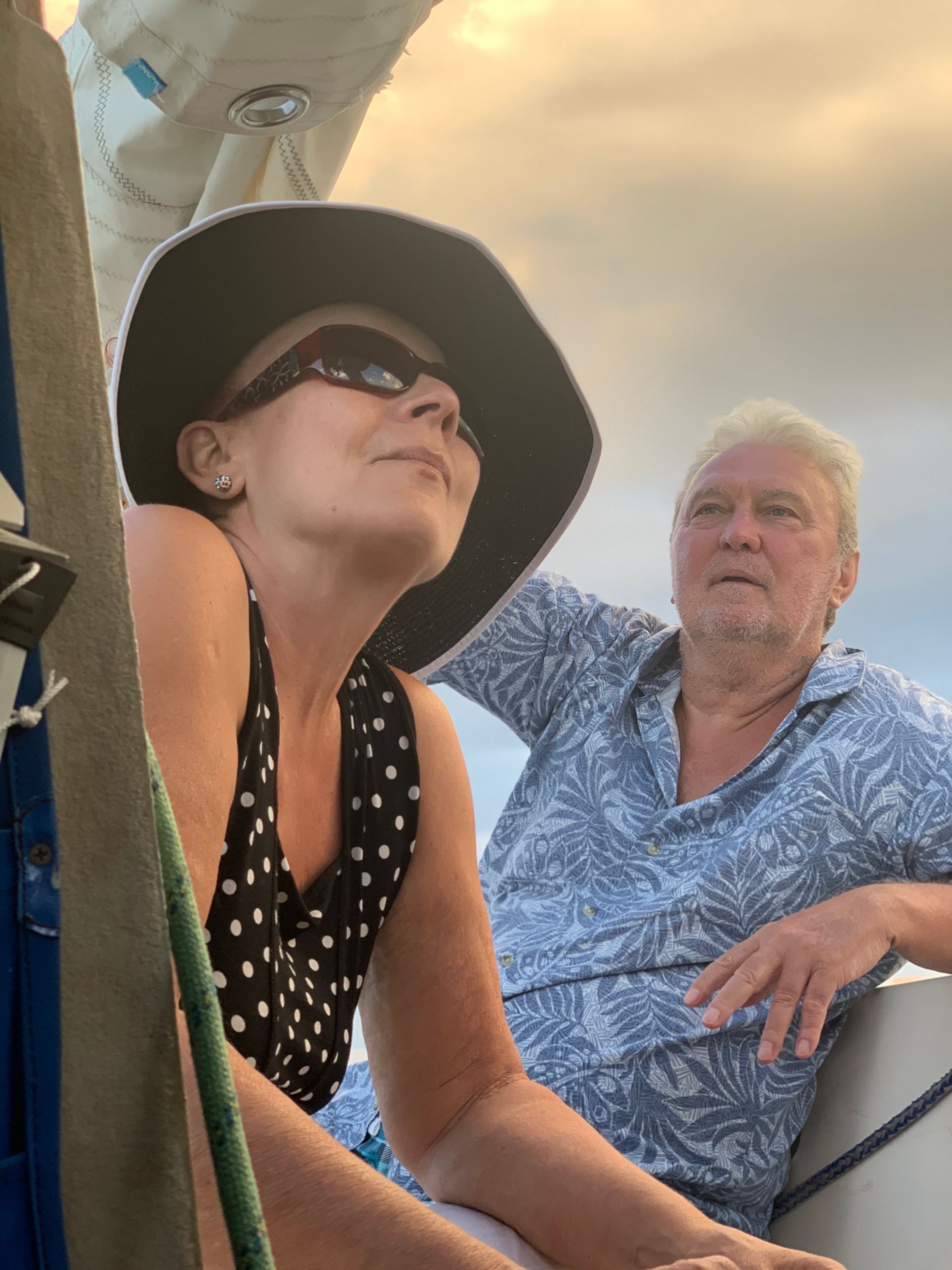 Woman in hat and sunglasses looks up on a boat; man in patterned shirt looks on.