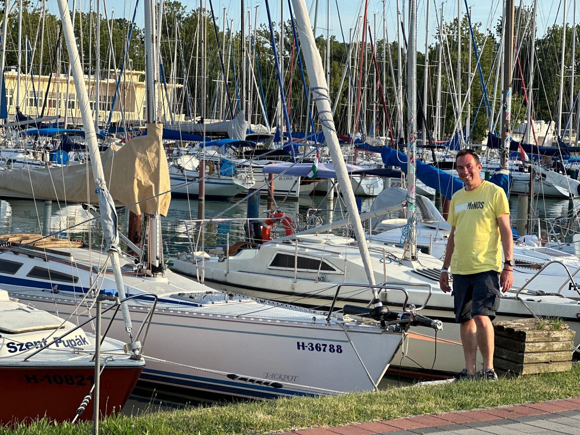 Man in yellow shirt stands near sailboats in a marina.