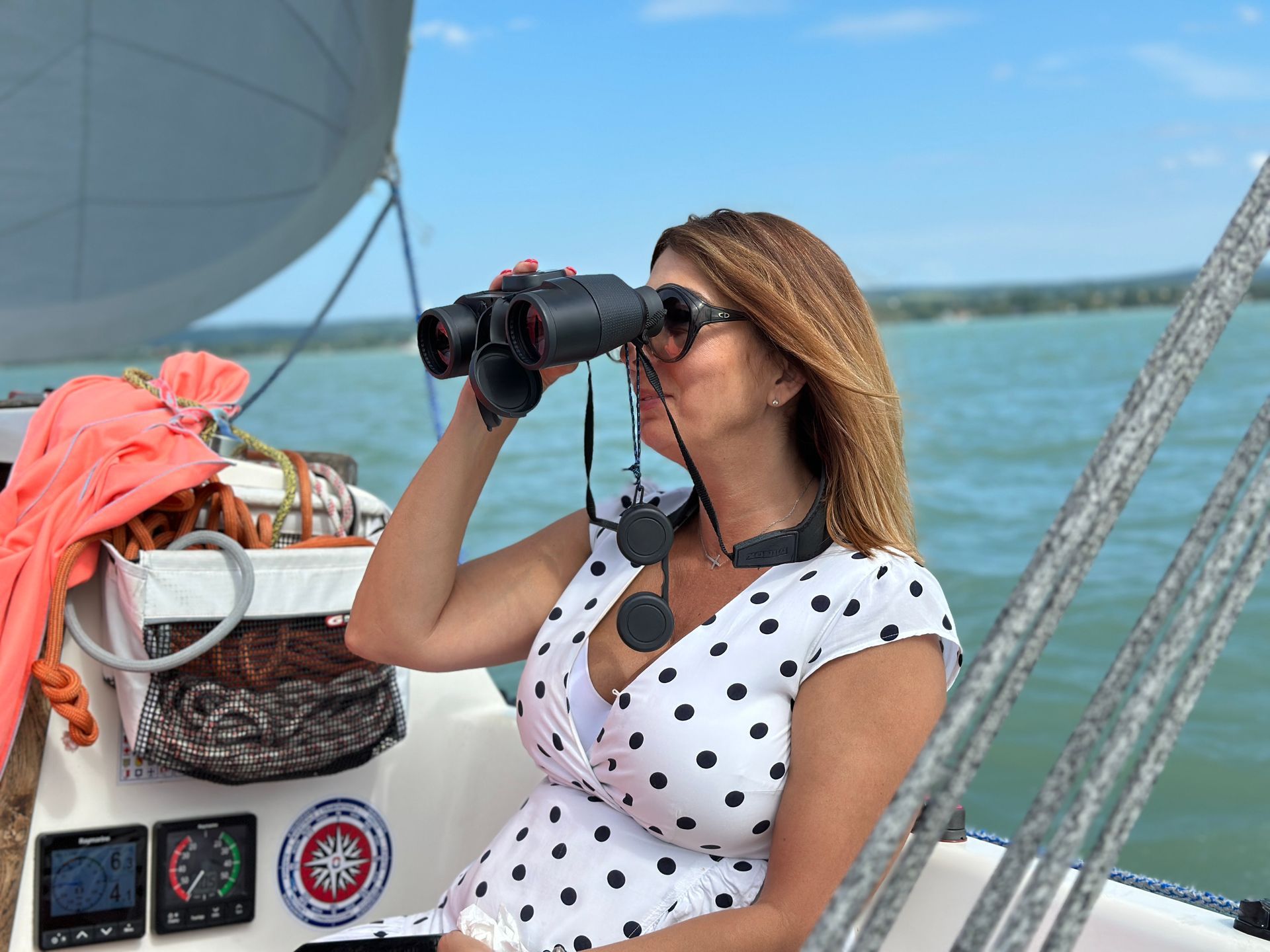 Woman on a sailboat looking through binoculars on a sunny day.