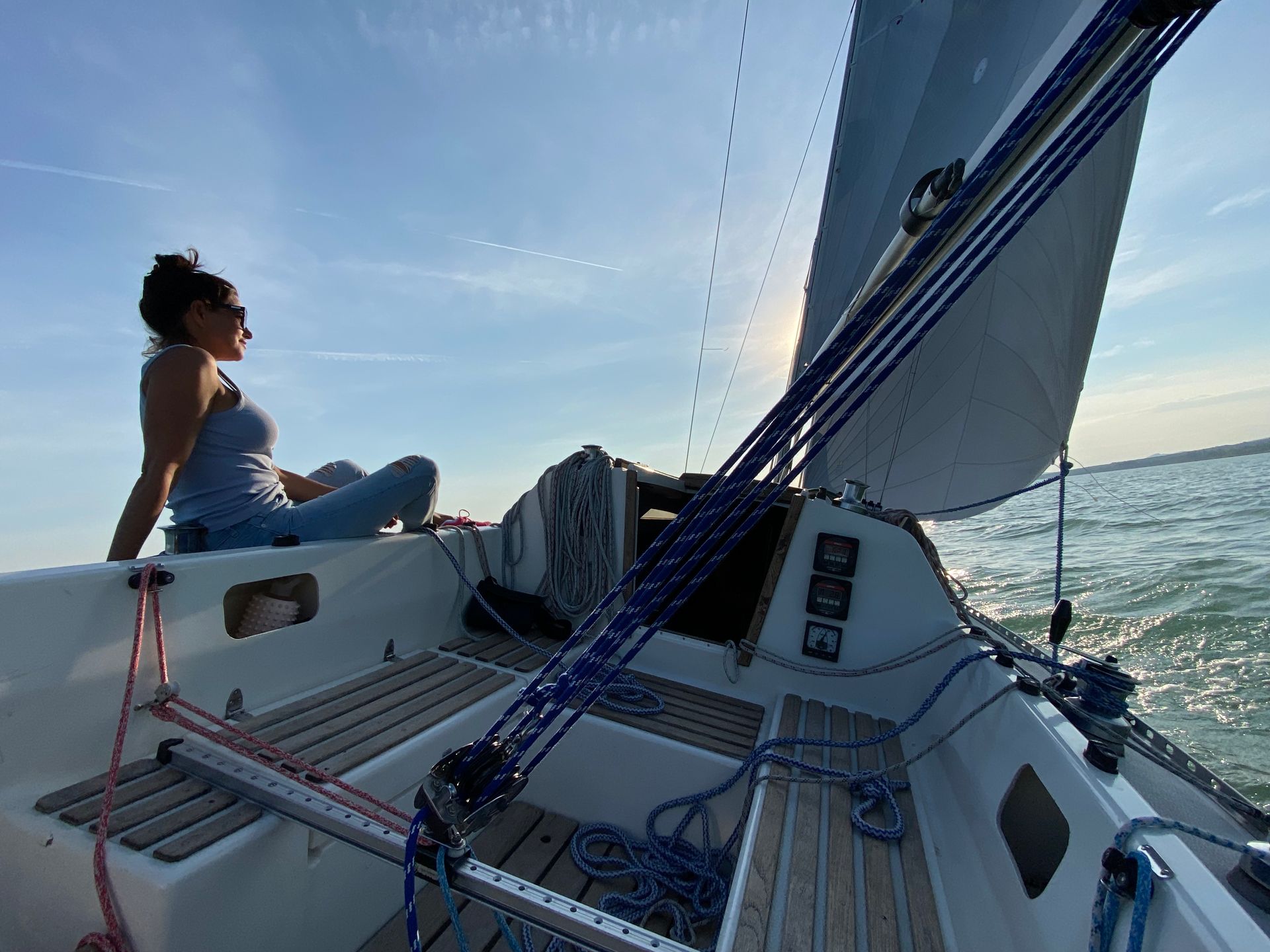 Woman on a sailboat, enjoying the sun. Blue sky, white sails, and ocean views.