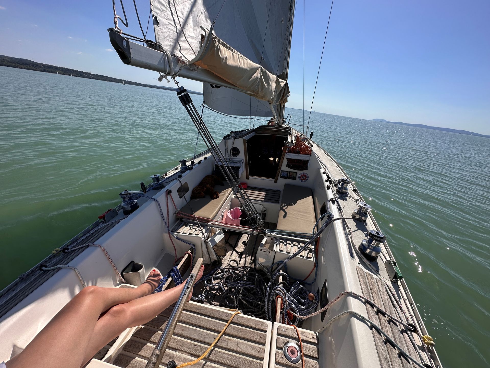 Sailboat on water with a person's hand holding a rope; blue sky and water; sunny day.