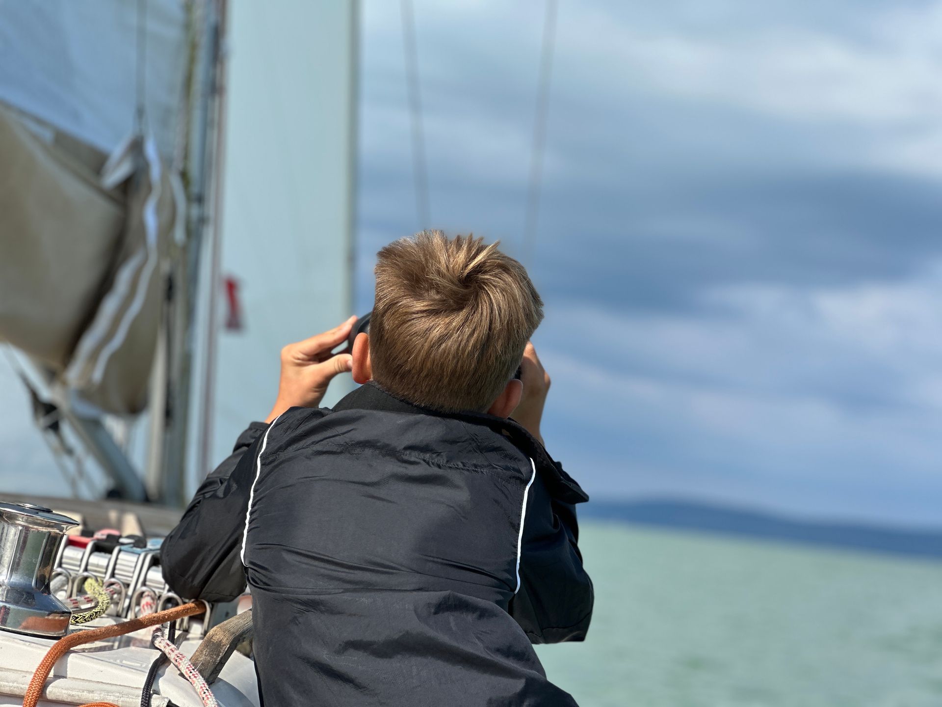 Person in a black jacket looking through binoculars from a boat on the water
