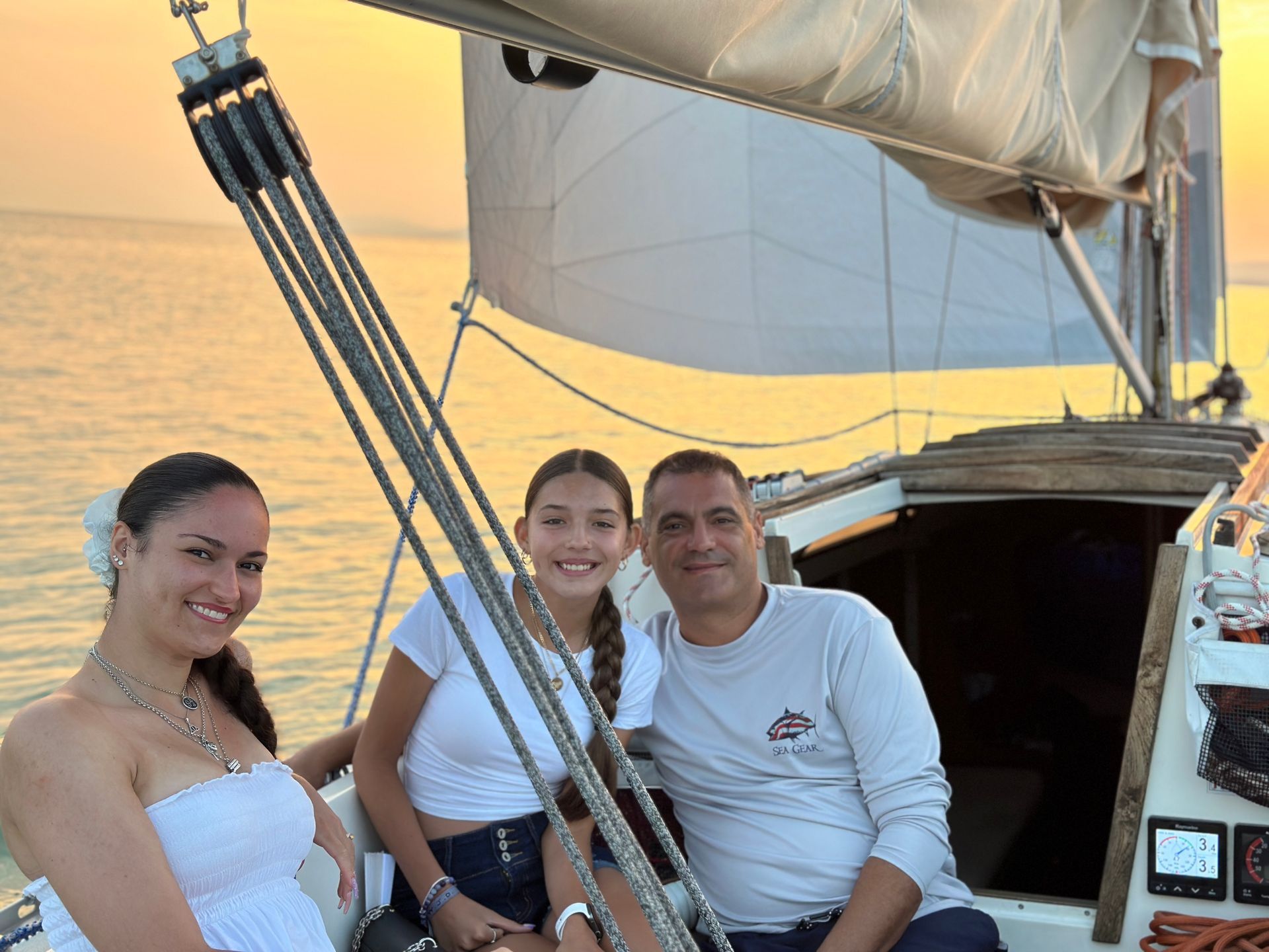 Family on a sailboat, smiling at sunset. White sails, warm colors, and ocean backdrop.