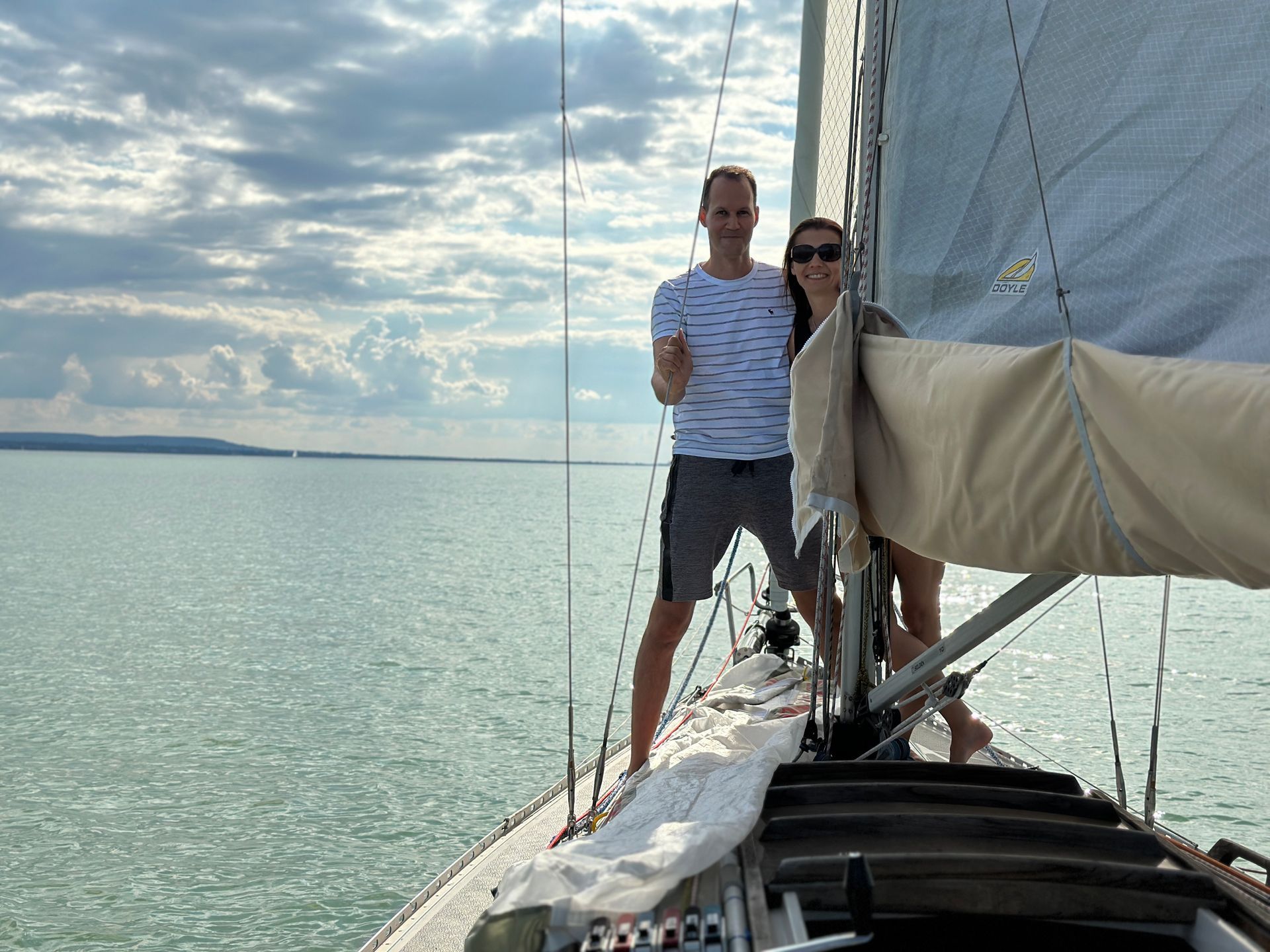 A couple on a sailboat, posing on the deck, with blue water and sky in the background.