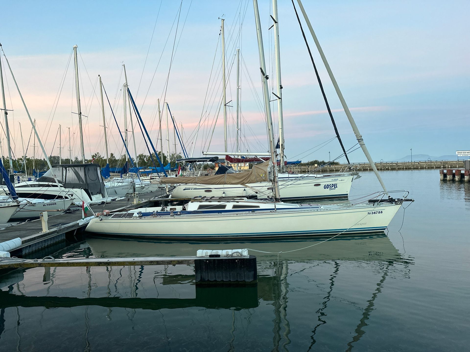 Sailboats docked in a harbor at dusk, reflecting in the calm water.