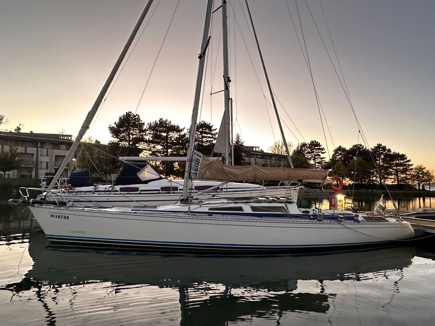 Sailboat docked at dusk, masts against the twilight sky, reflecting in still water.