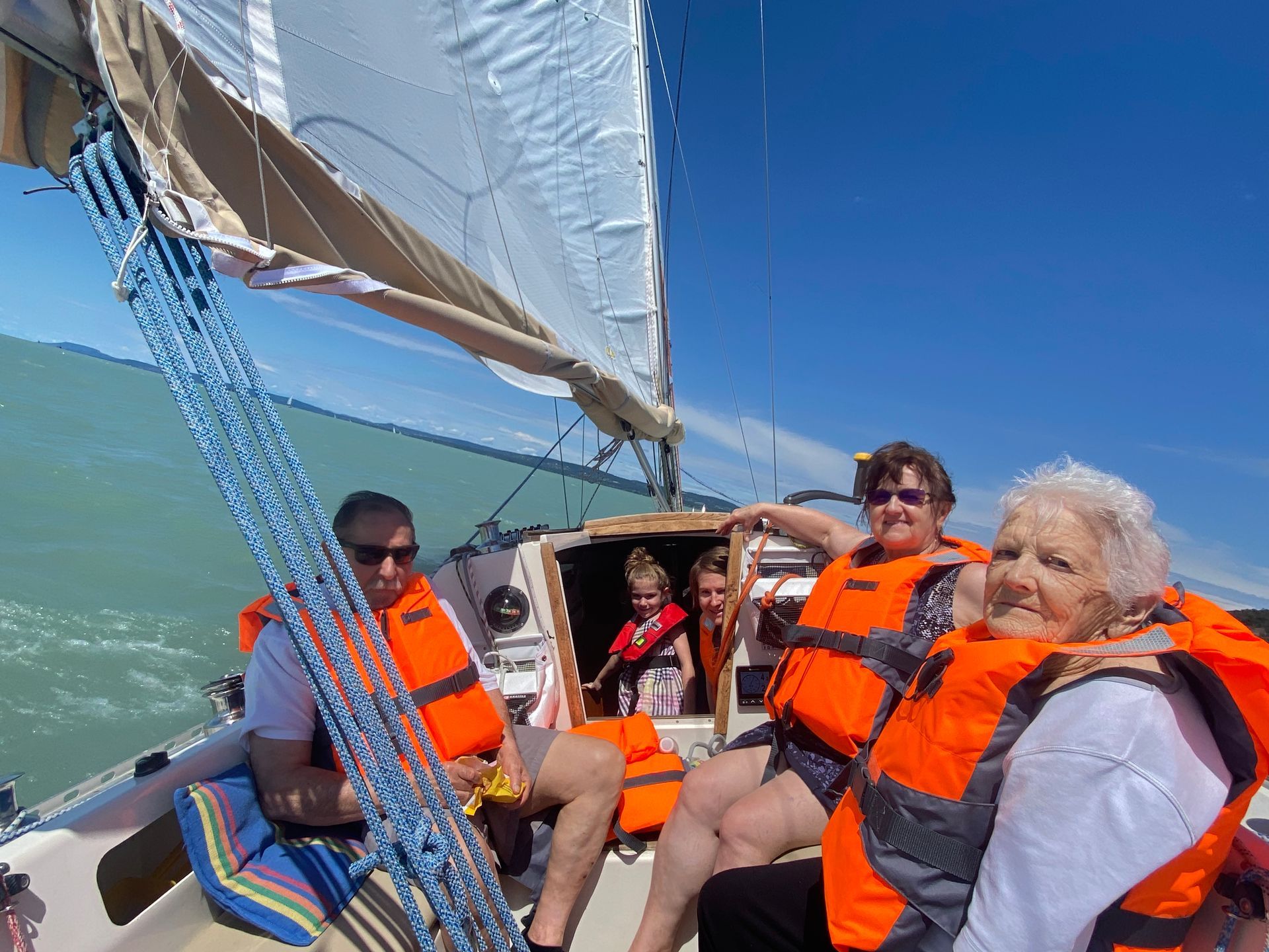 People wearing life vests on a sailboat, enjoying the sunny day on the water.