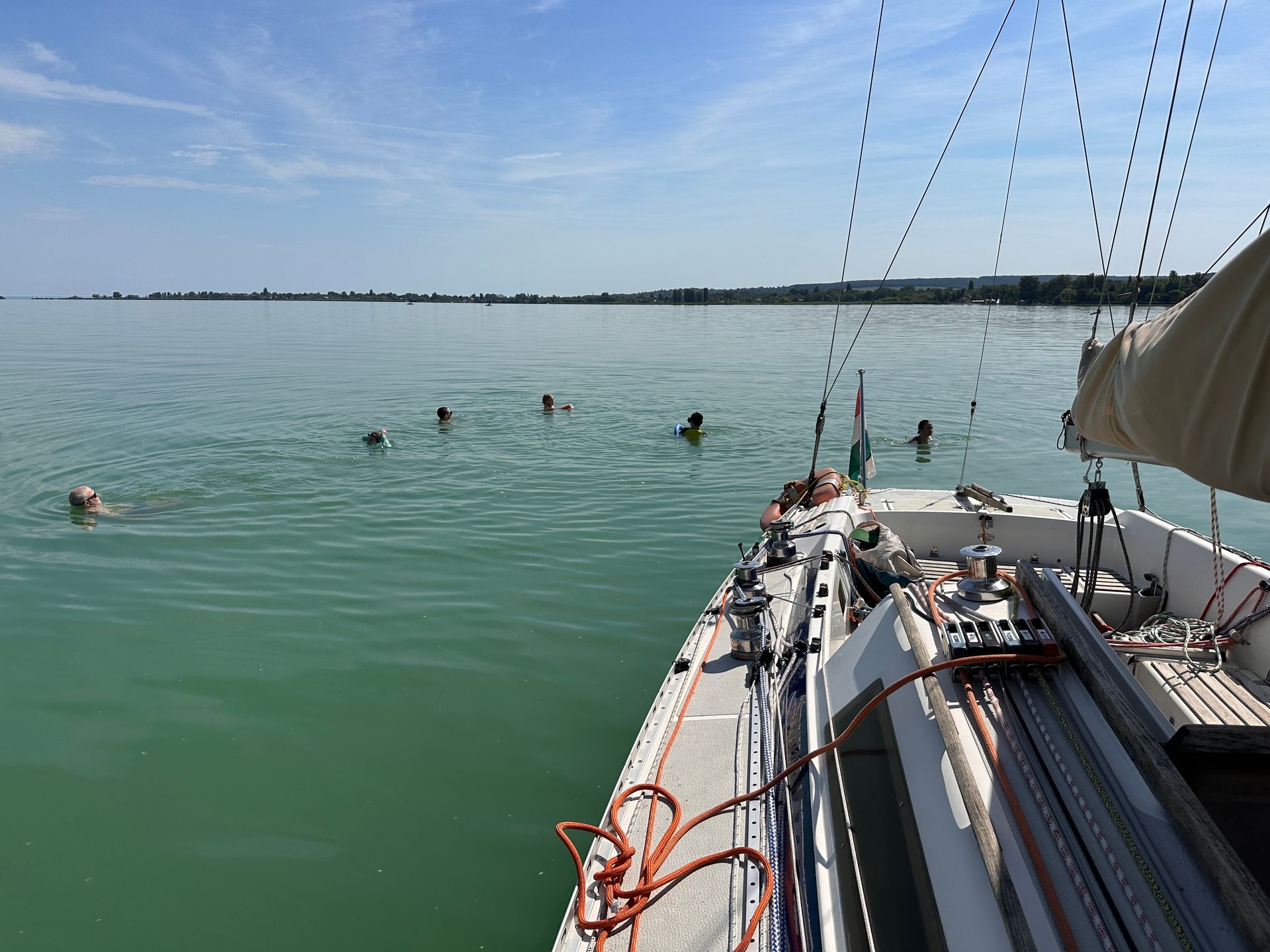 Sailboat with people swimming in turquoise water on a sunny day.