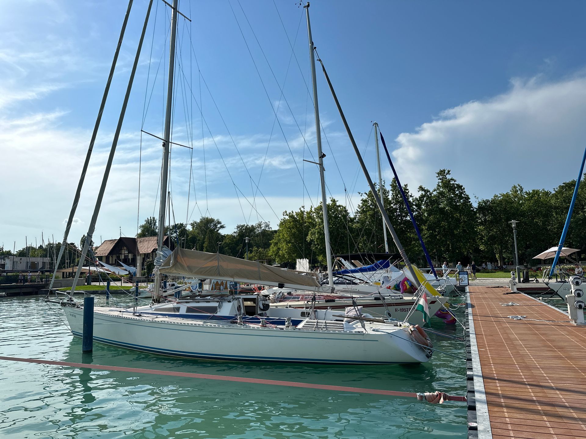 Sailboats docked at a pier on a sunny day, turquoise water, blue sky, trees in background.