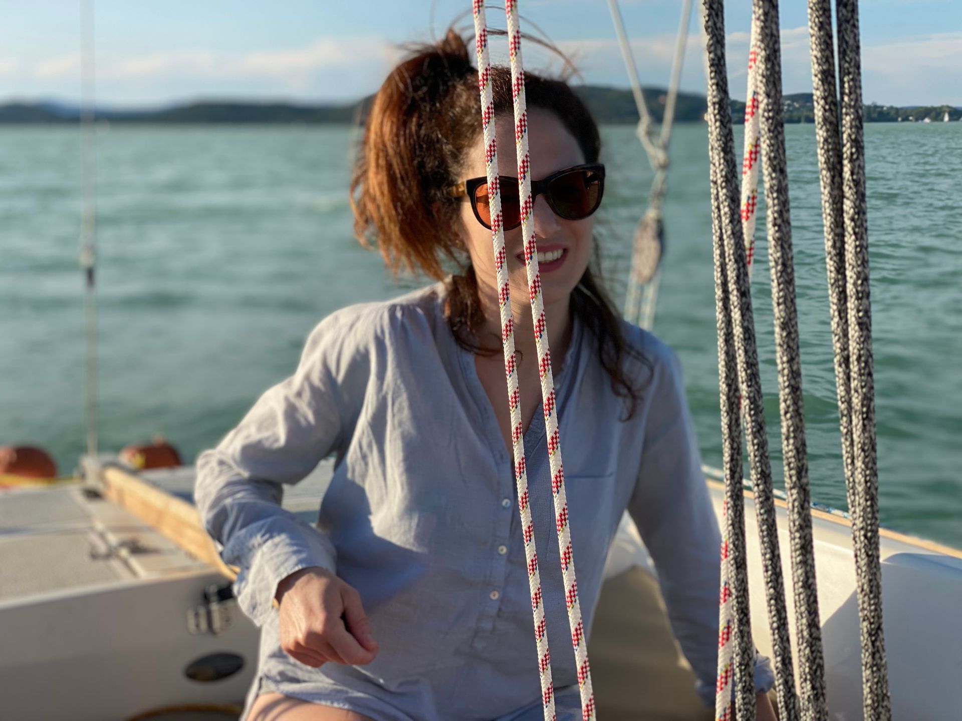 Woman with sunglasses smiles on a sailboat, looking towards the water.