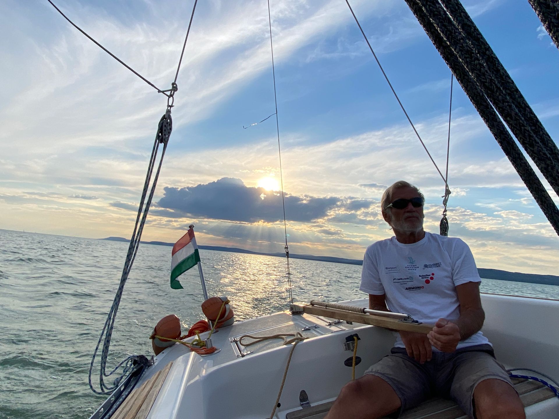 Man sailing a boat on a sunny day, Hungarian flag waving.