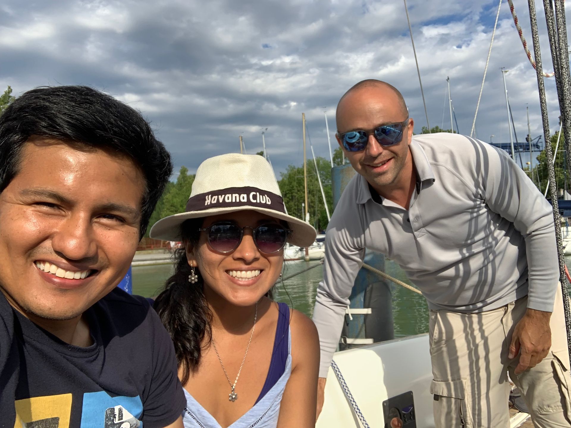 Three people smile for a selfie on a boat, lake, and sky in the background.