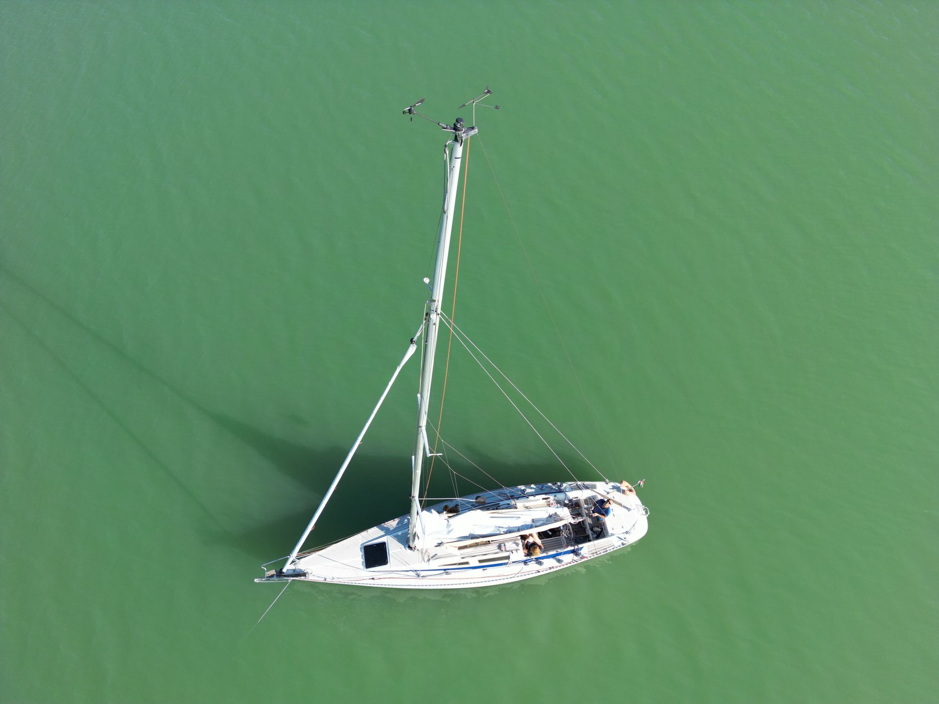 Sailboat on turquoise water. Overhead shot, long mast and shadows.