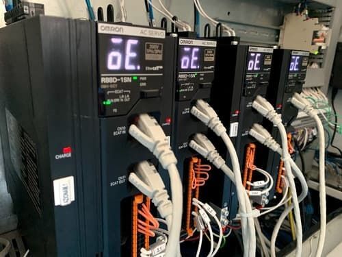 Una fila di servomotori industriali con display luminosi e cavi spessi in un quadro elettrico.