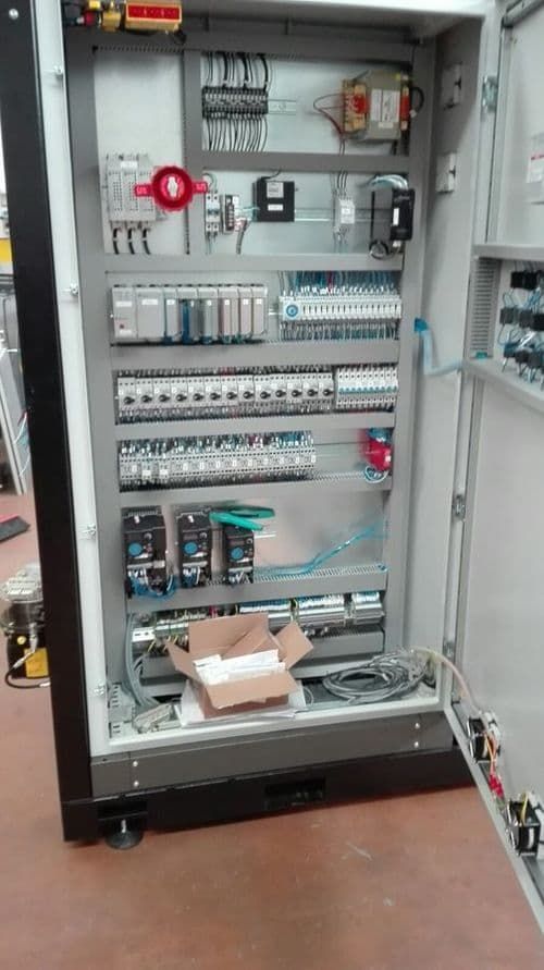 Quadro elettrico aperto con cablaggi, interruttori automatici e componenti all'interno di un armadio grigio.