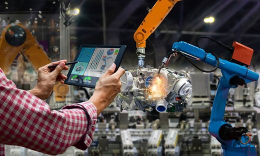Un tecnico tiene in mano un tablet in una fabbrica piena di robot, mentre bracci robotici assemblano i componenti.