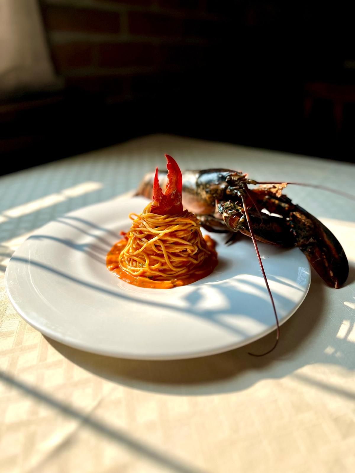 Piatto di spaghetti con chela di aragosta, aragosta accanto. Piatto bianco su un tavolo bianco.