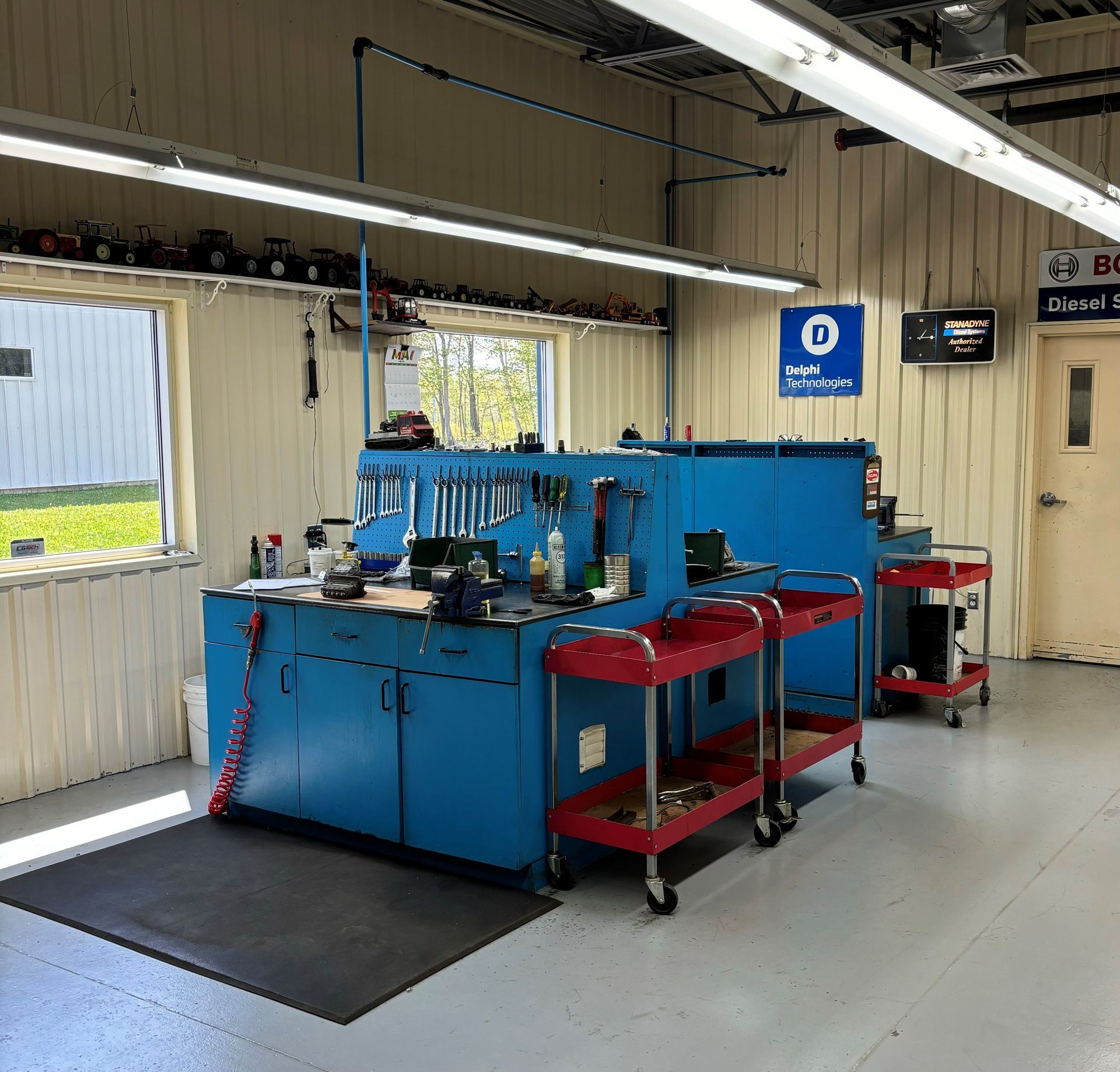 Machine industrielle bleue dans un atelier, avec des chariots et des outils rouges près d'un mur et d'une fenêtre