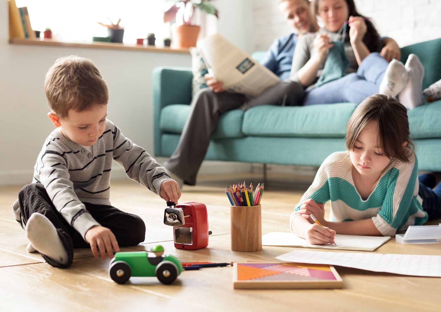 A family is sitting on a couch in a living room playing with toys.