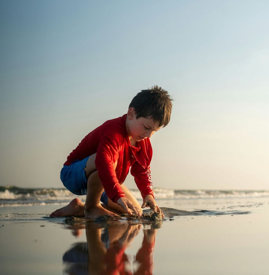 A young boy in a red shirt is playing on the beach