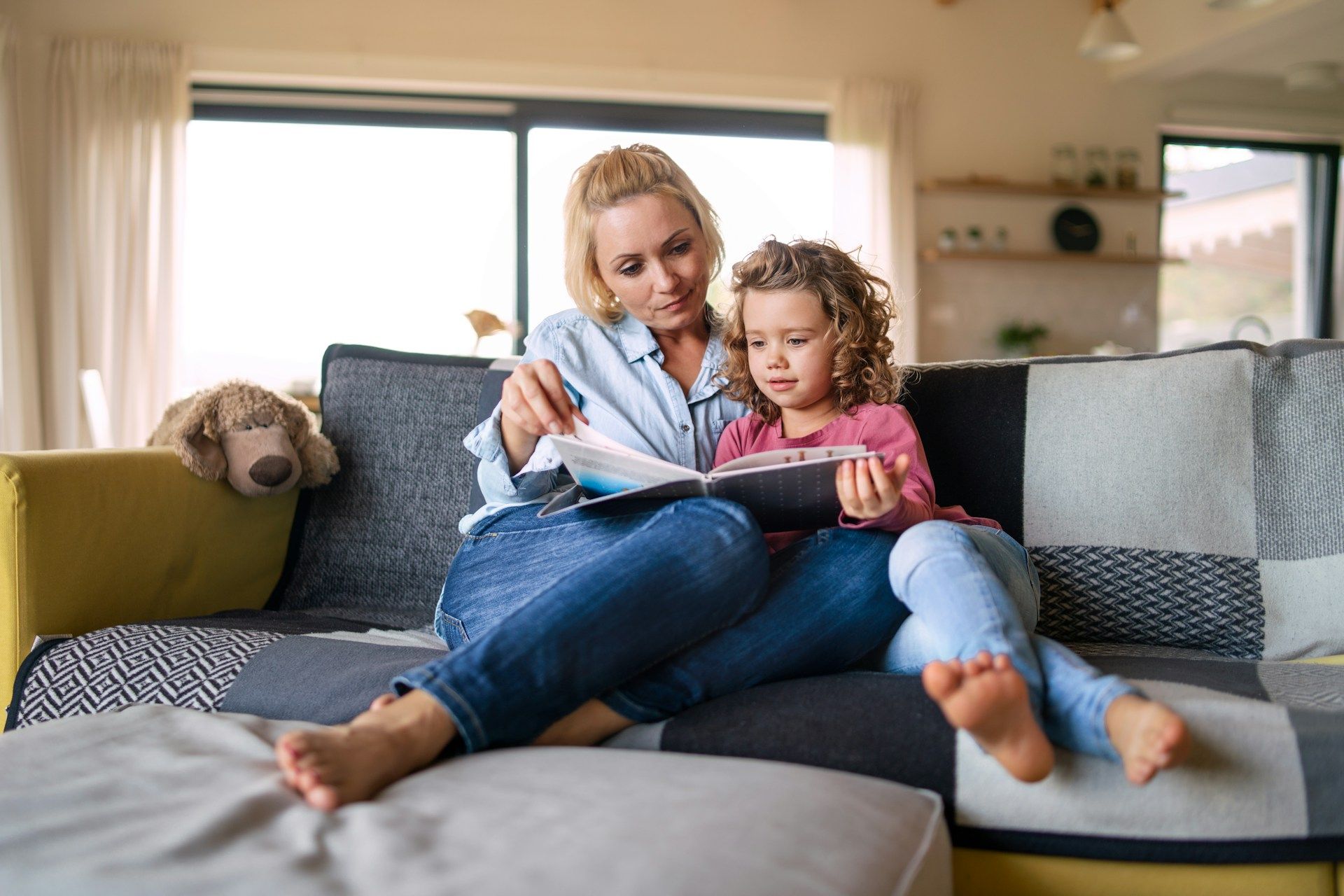 A woman and a little girl are sitting on a couch reading a book.