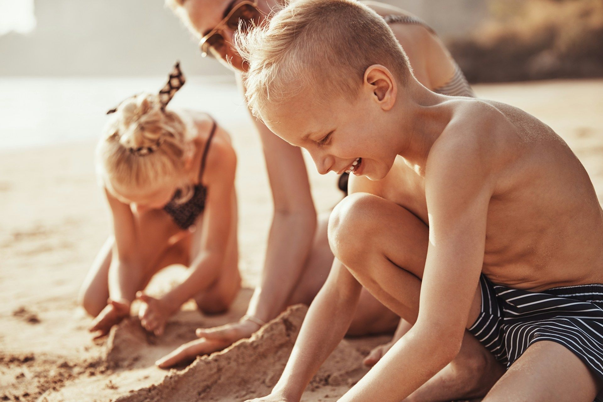 A woman and two children are playing in the sand on the beach.