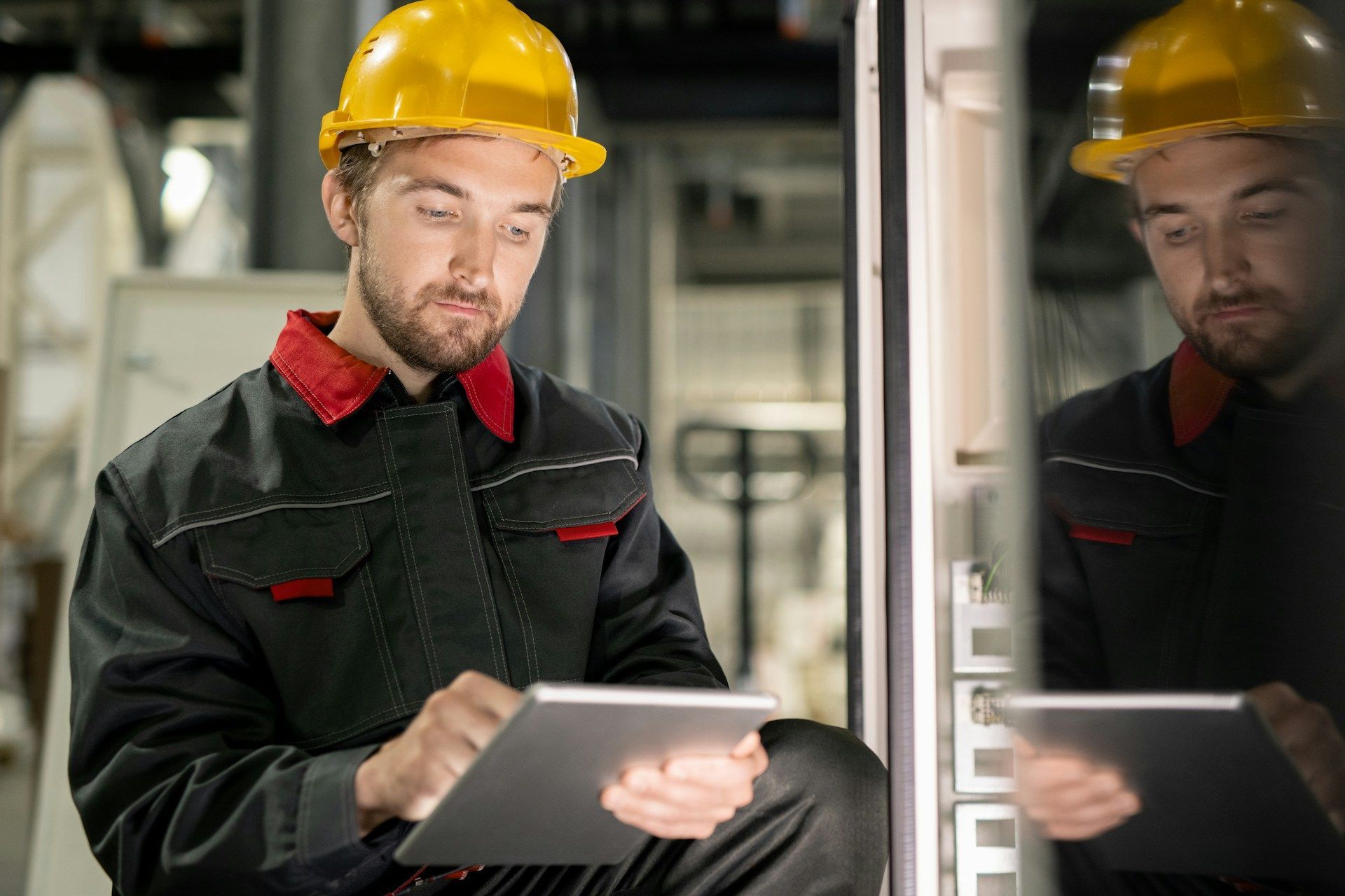 A man wearing a hard hat is using a tablet computer in a factory.