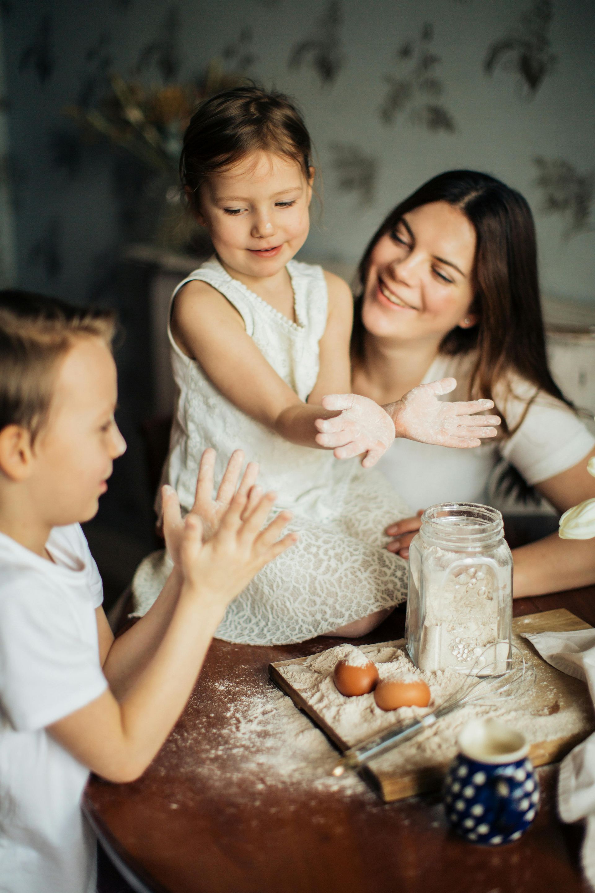 A woman and two children are playing with flour at a table.