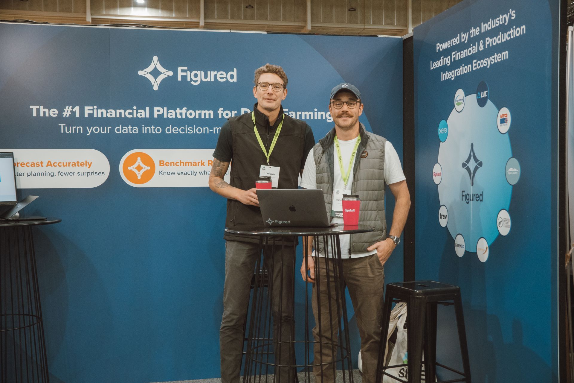 Two men stand at a booth promoting Figured, a financial platform for farming.
