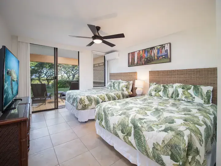 A hotel room with two beds , a flat screen tv and a ceiling fan.