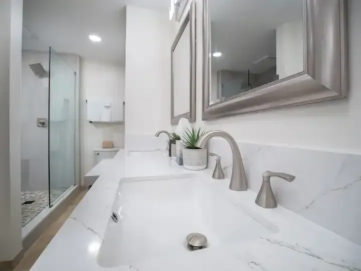 A bathroom with two sinks , a mirror and a walk in shower.
