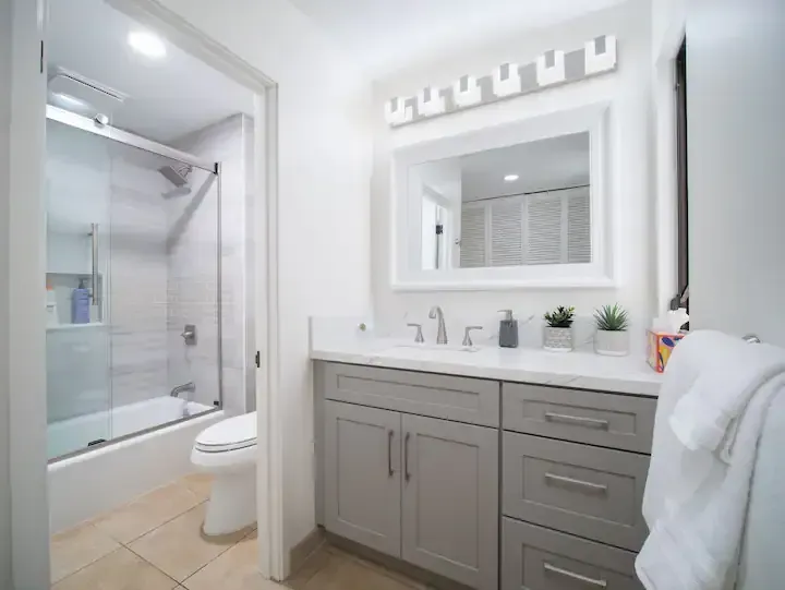 A bathroom with a toilet , sink , mirror and shower.
