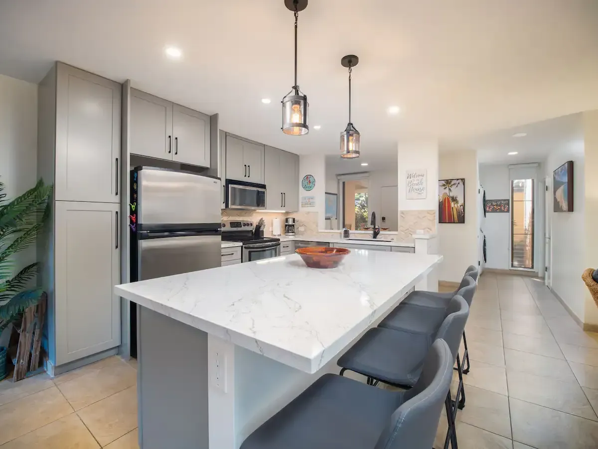 A kitchen with a large island , stools and a refrigerator.