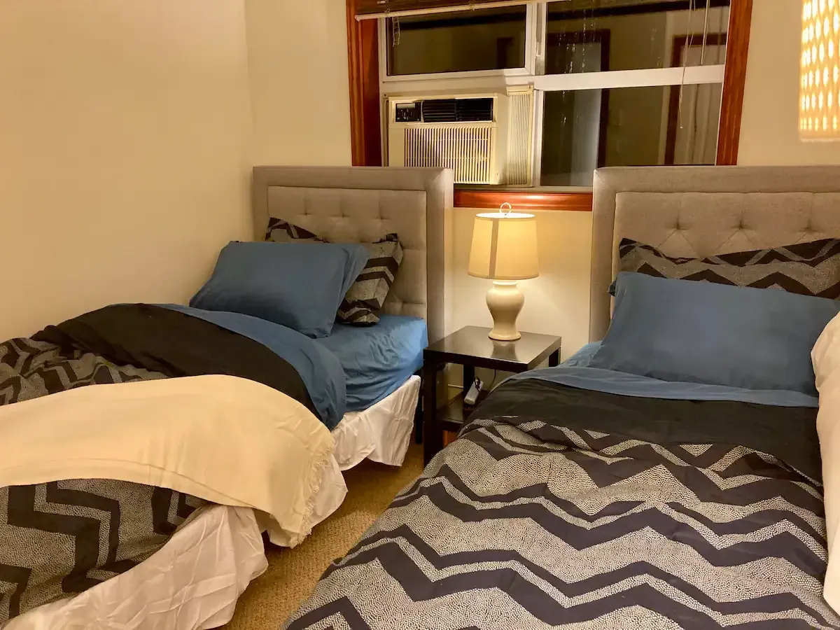 A bedroom with two beds , a lamp and a window.